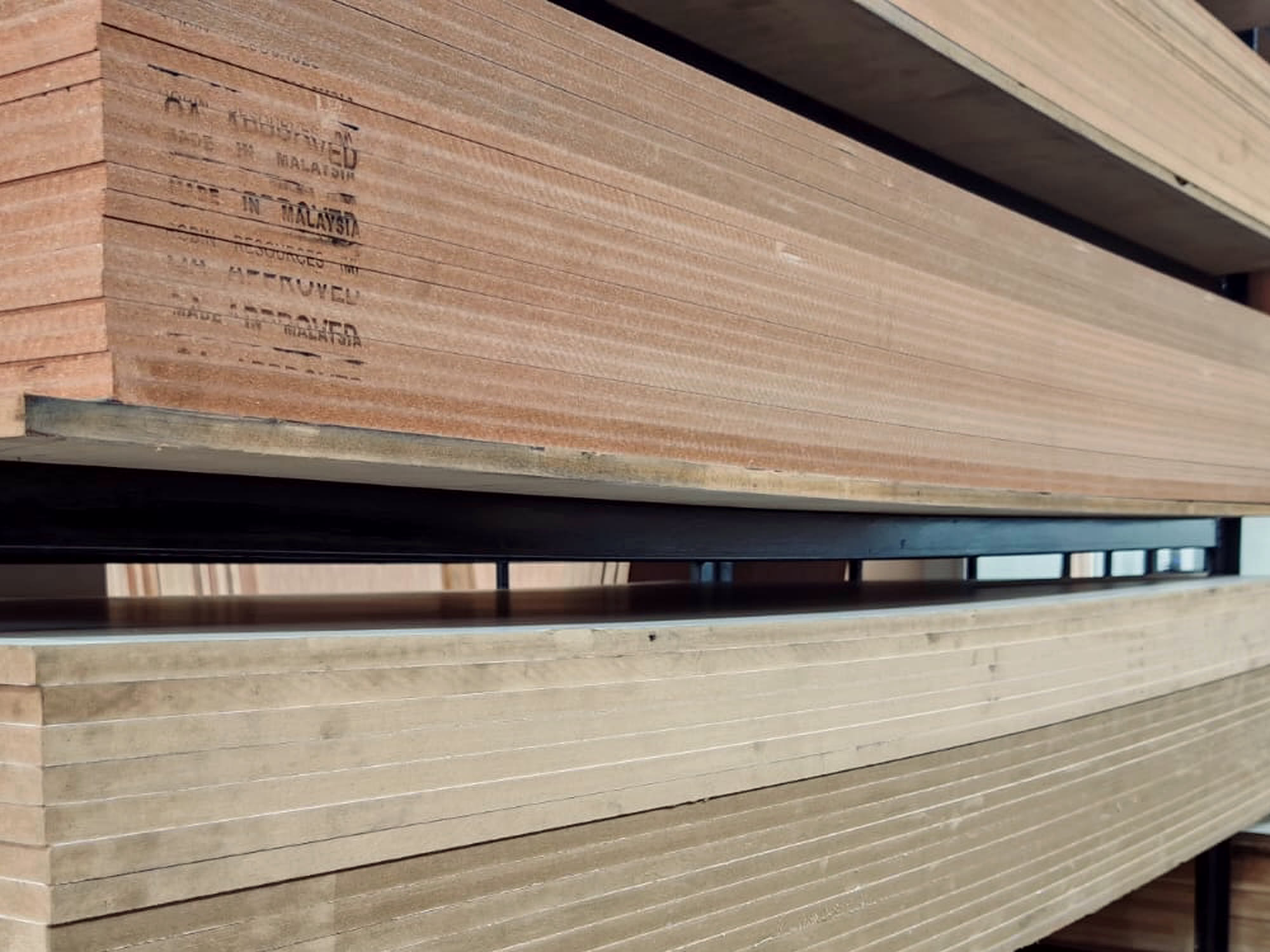 Mill stamps reading MADE IN MALAYSIA and QA APPROVED printed across the edges of a stacked plywood bundle.