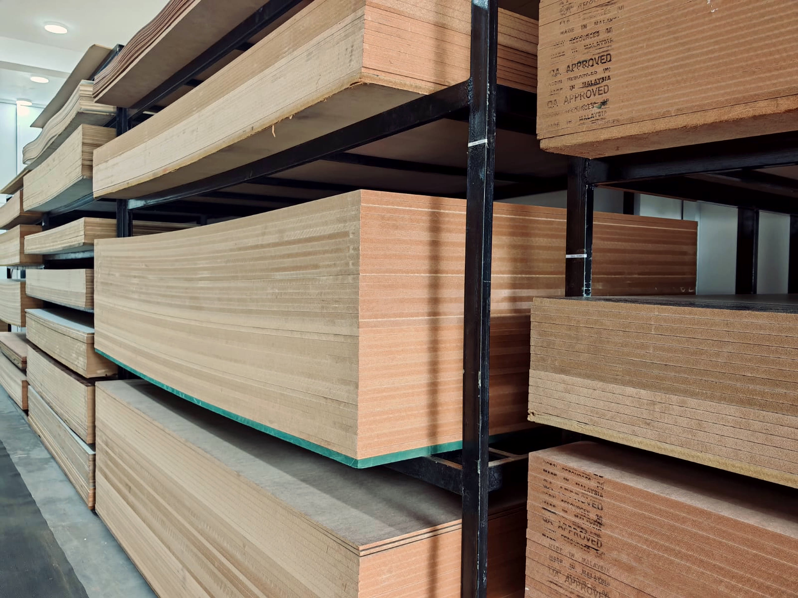 Board edges at close range on black steel racking, including a green edged moisture resistant sheet and QA APPROVED stamps.