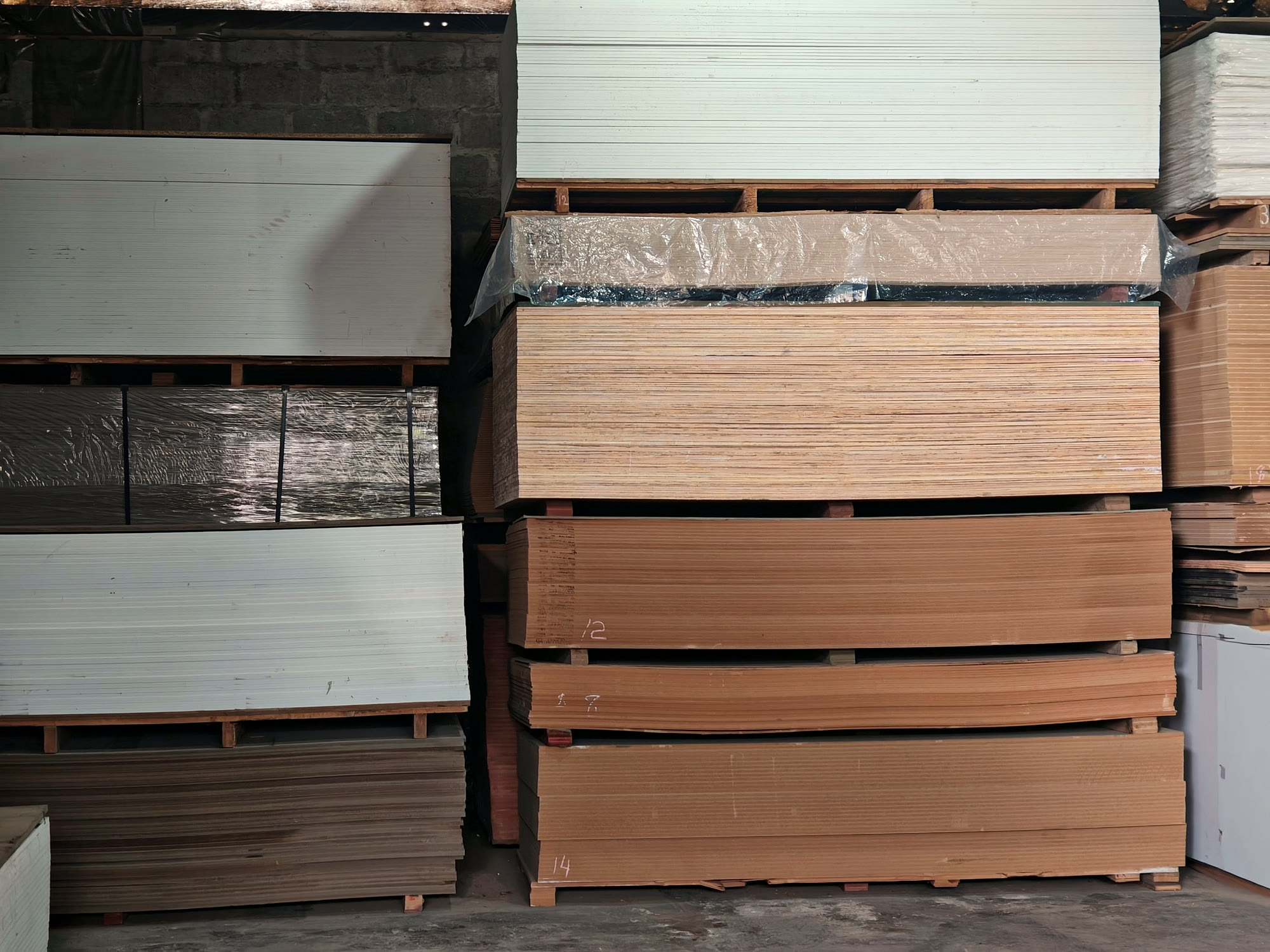 Floor to roof pallet stacks of white boards, plywood and MDF, chalk marked with their thicknesses.
