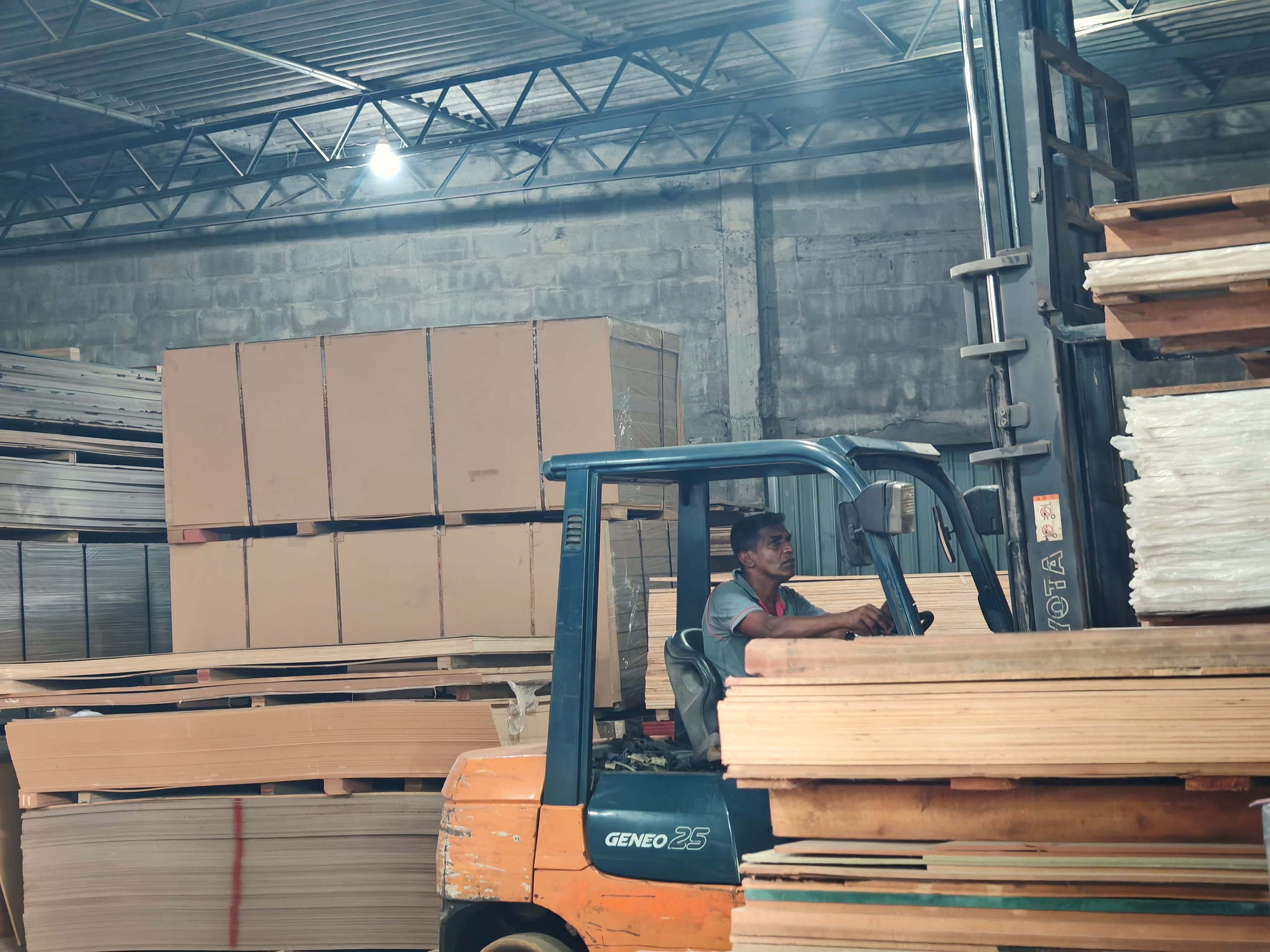 A forklift carrying a stack of plywood sheets across the warehouse.
