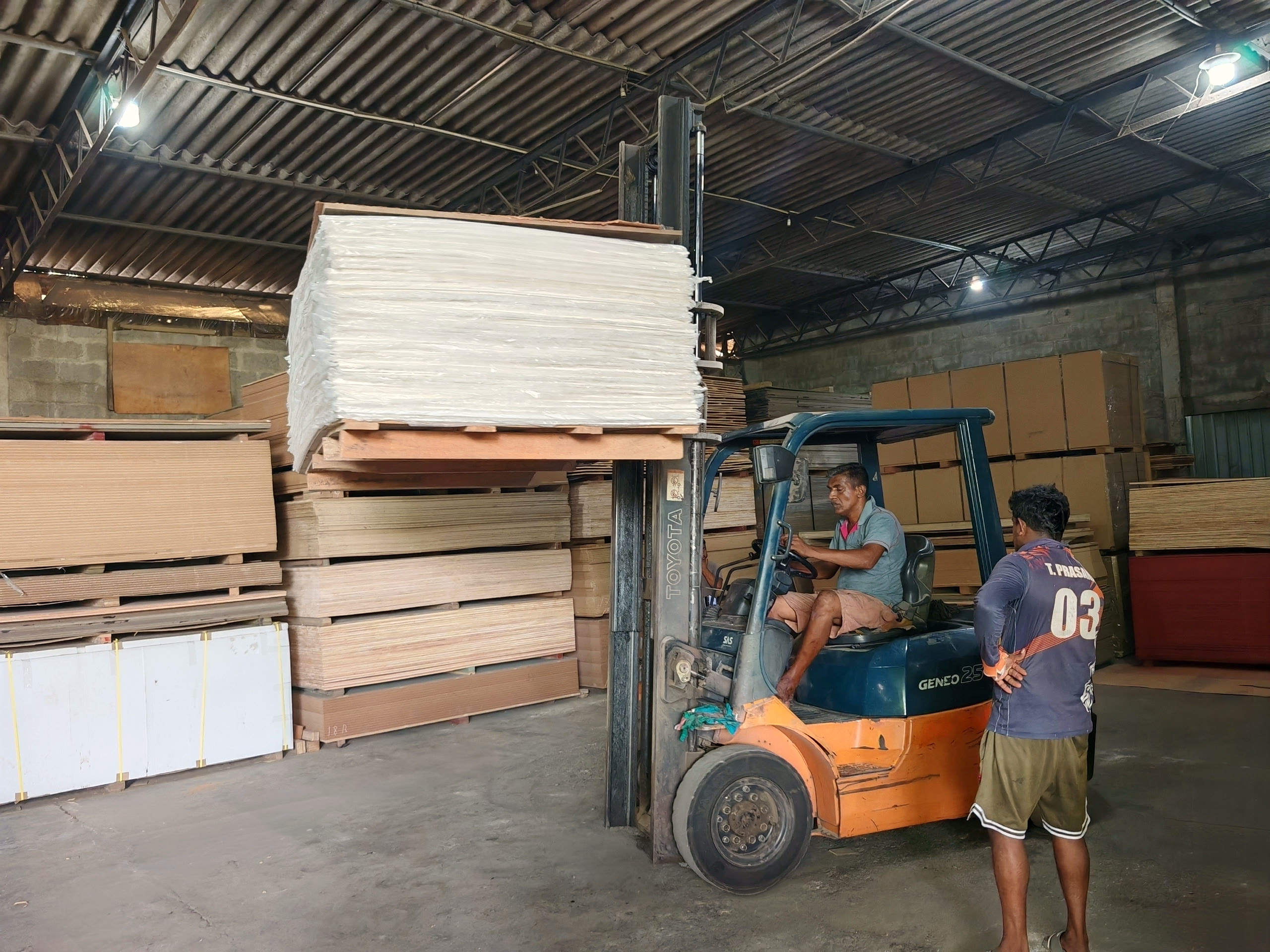 A forklift lifting a full pallet of white faced sheets high off the stack in the warehouse.
