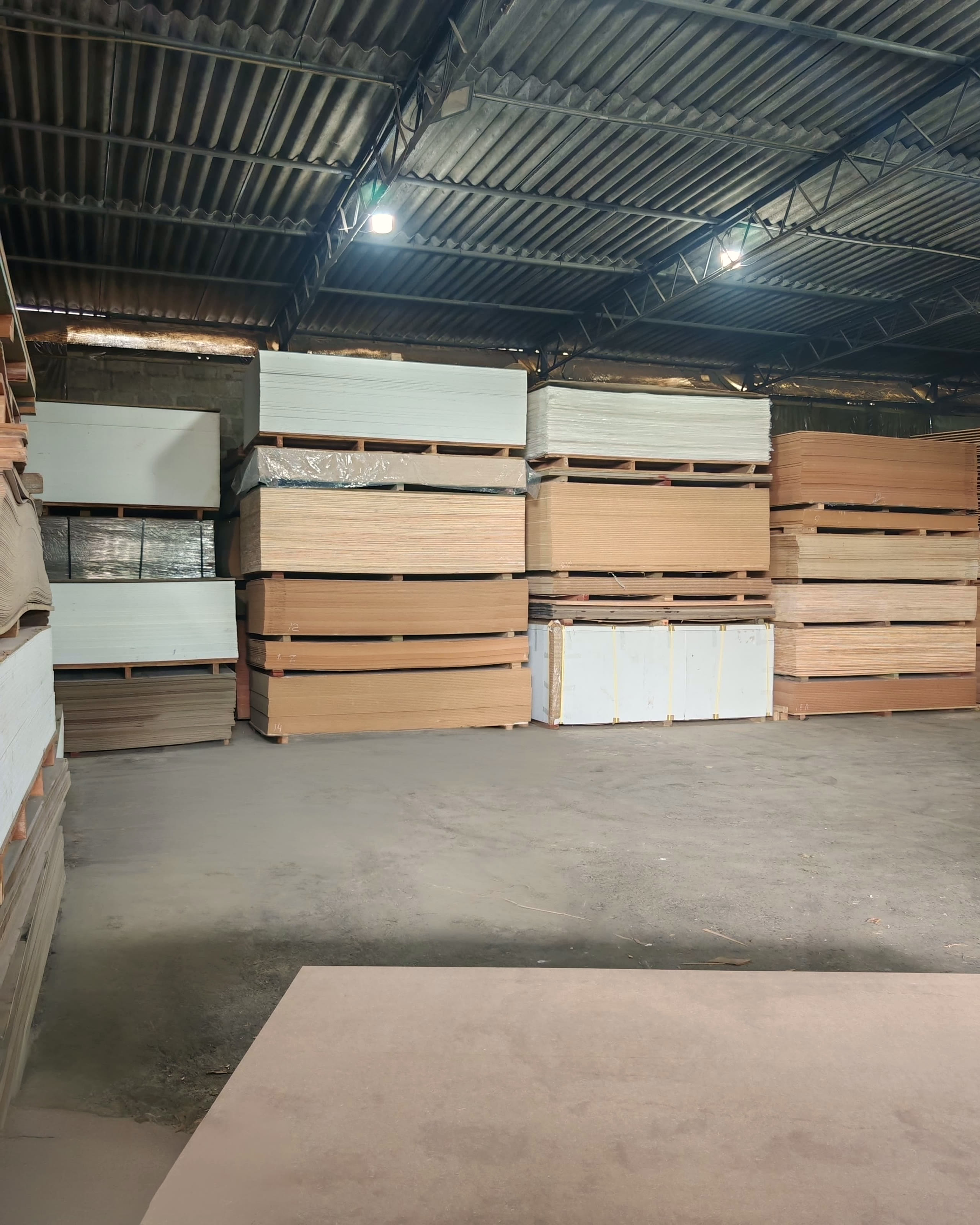 Palletised stacks of plywood, MDF and faced boards under the warehouse roof.